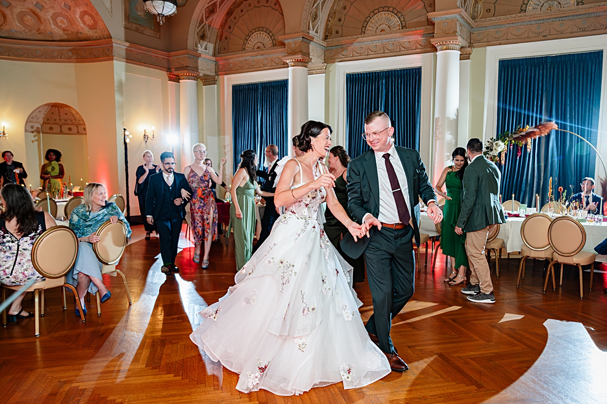 bride and groom walk onto the dance floor holding hands at their wedding reception in Christman Hall at Stambaugh Auditorium in Youngstown OH.